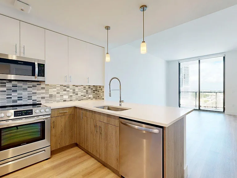 Apartment Kitchen with Stainless Steel Appliances, Dining and Living Room with Wood Style Flooring.