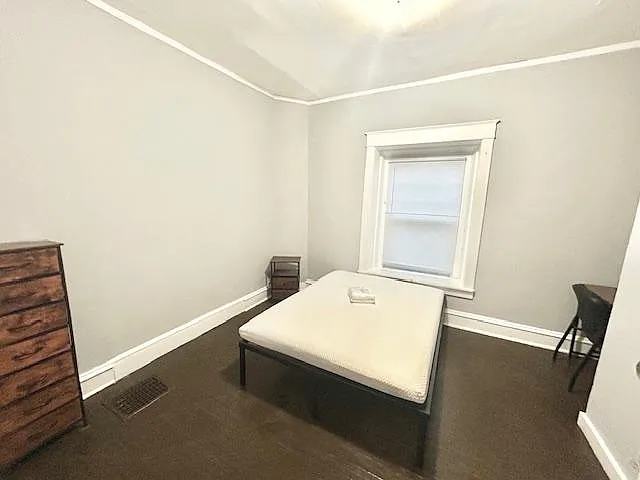 Private bedroom with a bed, dresser, and workspace, plus a window with blinds and neutral finishes for easy move-in.