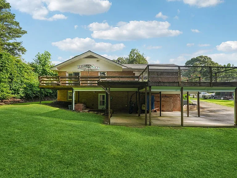This charming rear view showcases a spacious deck, covered lower patio, and storybook greenery, offering wonderful outdoor flexibility with a private woodland feel.
