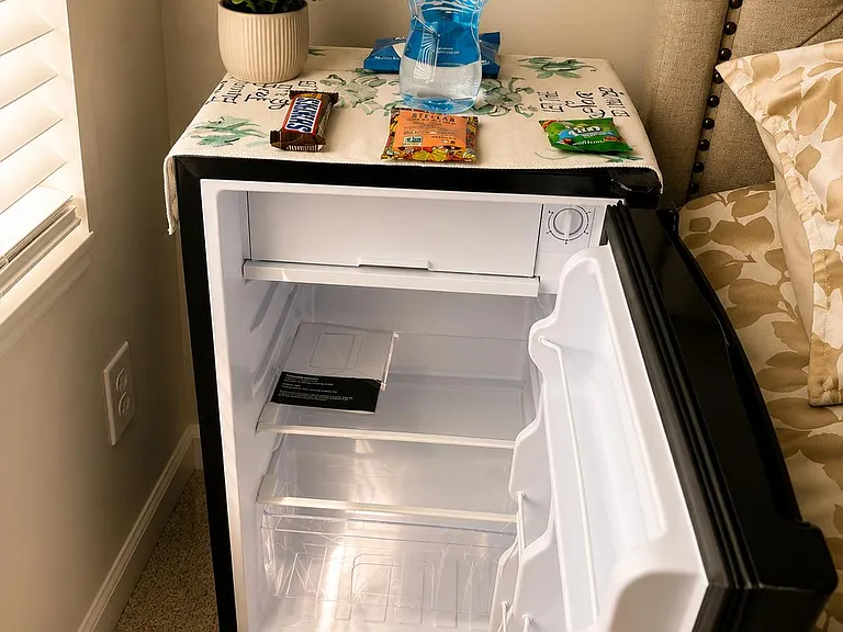 In-room mini fridge provides convenient cold storage for drinks and snacks, paired with a bedside surface for essentials.
