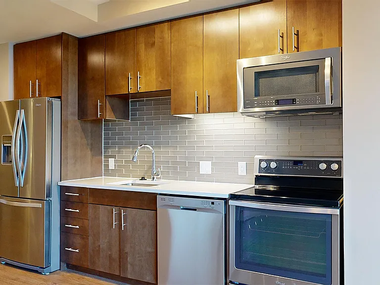 Apartment kitchen with stainless steel appliances, quartz countertops and wood-style flooring.
