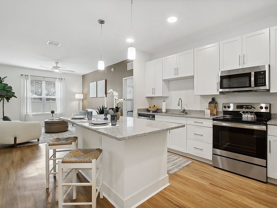 Modern apartment featuring a bright open kitchen with sleek white cabinets and stainless steel appliances, seamlessly flowing into an inviting living area with stylish decor and abundant natural light.