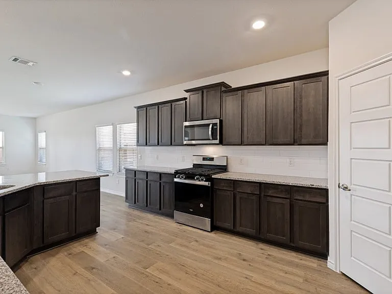 Modern kitchen featuring dark wood-finish cabinetry, light-colored speckled countertops, a stainless steel gas range, and a built-in microwave