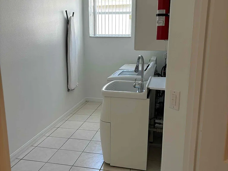 Laundry room fully equipped with a new washer, dryer, utility sink, and storage cabinets
