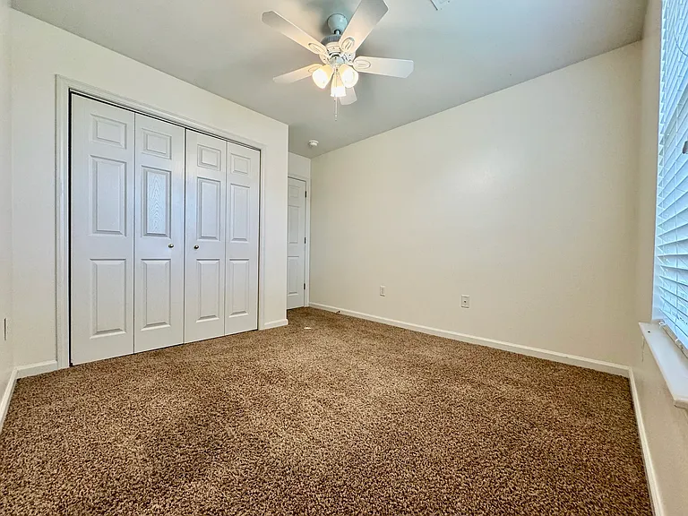 Third bedroom with ceiling fan, closet, and natural light
