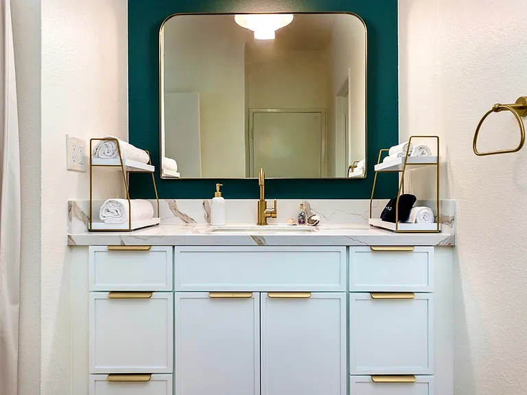 Modern bathroom vanity with marble countertop, gold fixtures, and designer lighting.