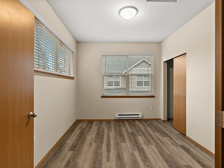 Light-filled bedroom featuring modern flooring, large windows, and a convenient closet with sliding doors. Light-filled bedroom featuring modern flooring, large windows, and a convenient closet with sliding doors.
