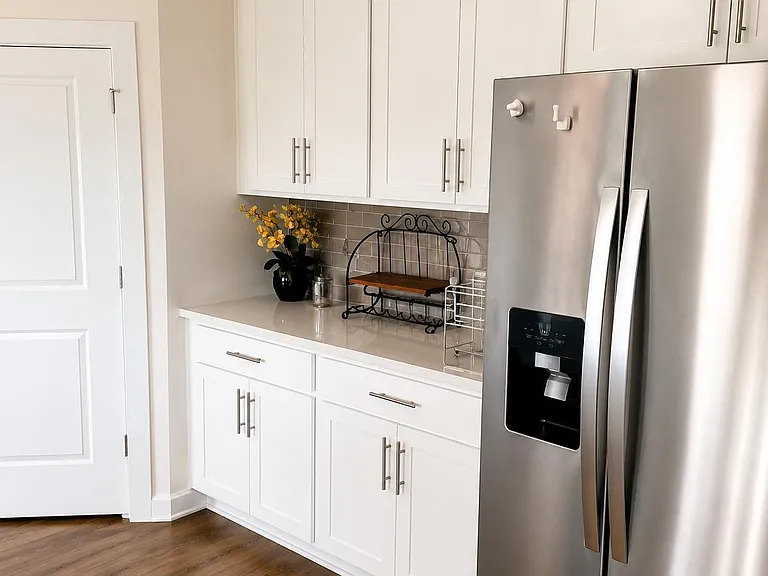 Kitchen features white cabinetry, ample counter space, and a stainless side-by-side refrigerator with water/ice dispenser.