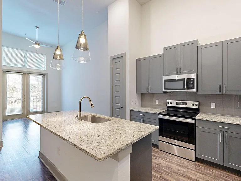 Apartment Kitchen with Stainless Steel Appliances, Dining and Living Room with Wood Style Flooring.