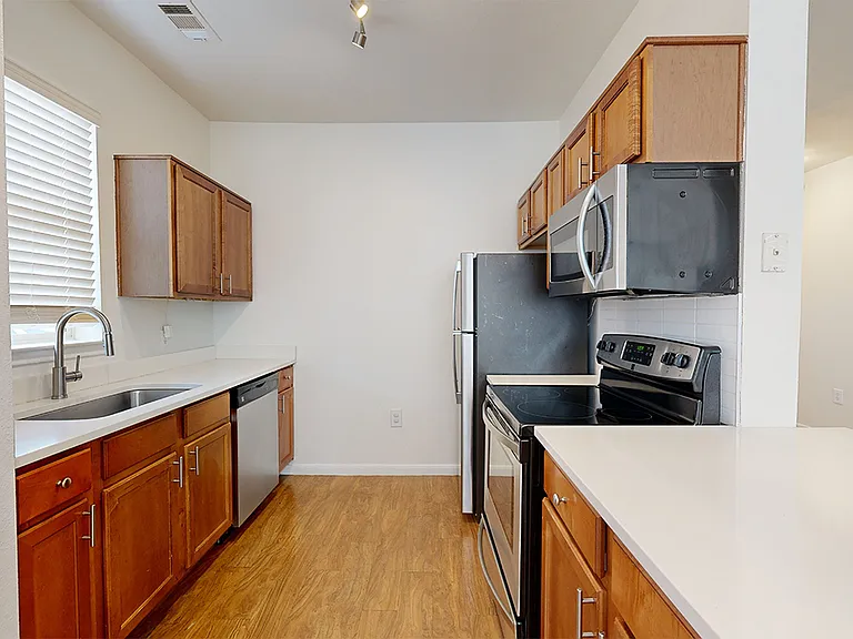 Apartment kitchen with stainless steel appliances and wood-style flooring. Quartz-style countertops (shown here) are available in select homes.