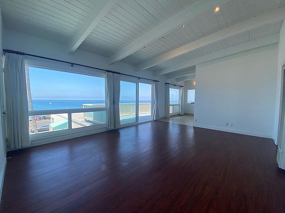 The living room is spacious with incredible ocean views and gorgeous wood floors and white beamed ceilings
