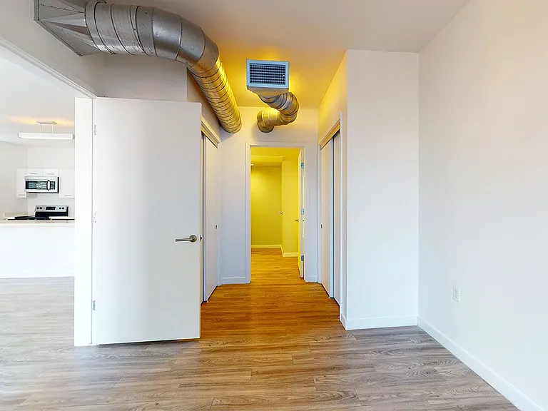 Spacious apartment bedroom with attached bathroom and wood-style flooring.