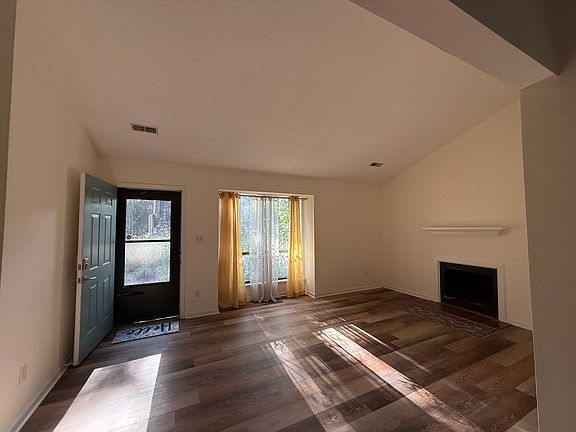 The spacious living room has a cathedral ceiling, natural light, snap light, and decorative fireplace. Sheer and mid-weight curtains are provided.