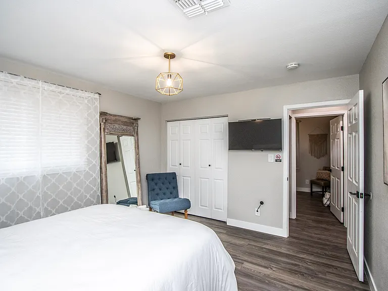 Cozy bedroom view at Casa Del Sol, Tempe rental home. Showcases a flat-screen smart TV, a plush blue accent chair, bi-fold closet doors, geometric lighting, and a rustic full-length mirror. Comfortable accommodation for a top Tempe, AZ vacation.