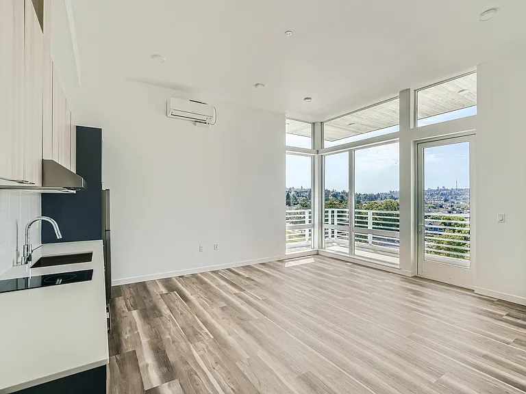 Experience the open layout of this modern kitchen and living room at Anker Ballard, featuring hardwood floors and a stunning city view.
