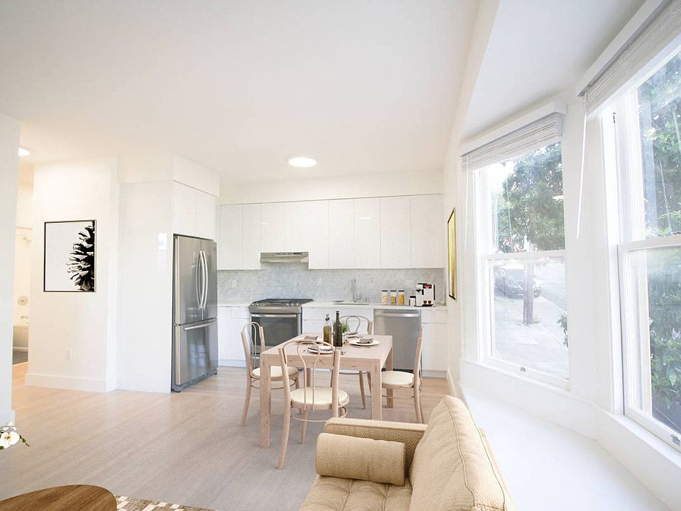 Kitchen and dining area with refrigerator. sink, and stove, with a large window, wooden table with four chairs, and sofa