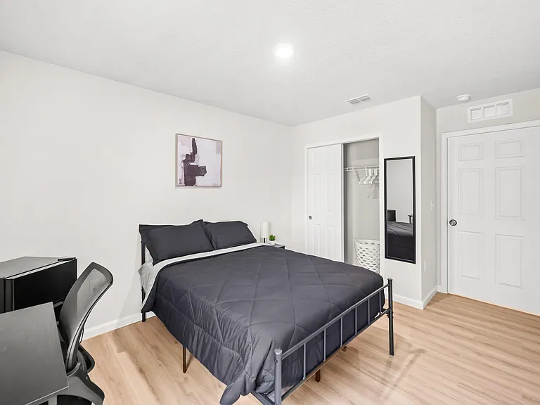 Private furnished bedroom with a full bed, desk space, and an open closet with hanging storage for easy organization.