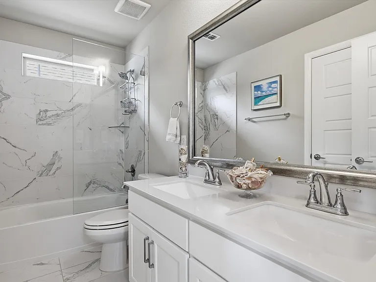 Upstairs bathroom featuring a double vanity with white cabinetry, polished chrome faucets, and a white countertop, along with a beautifully designed shower with a partial glass enclosure.