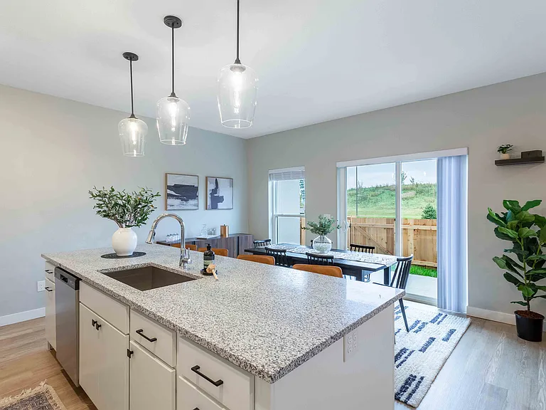 Modern open-concept kitchen and dining area with elegant pendant lighting, spacious island, and large sliding glass doors leading to a lush outdoor view.