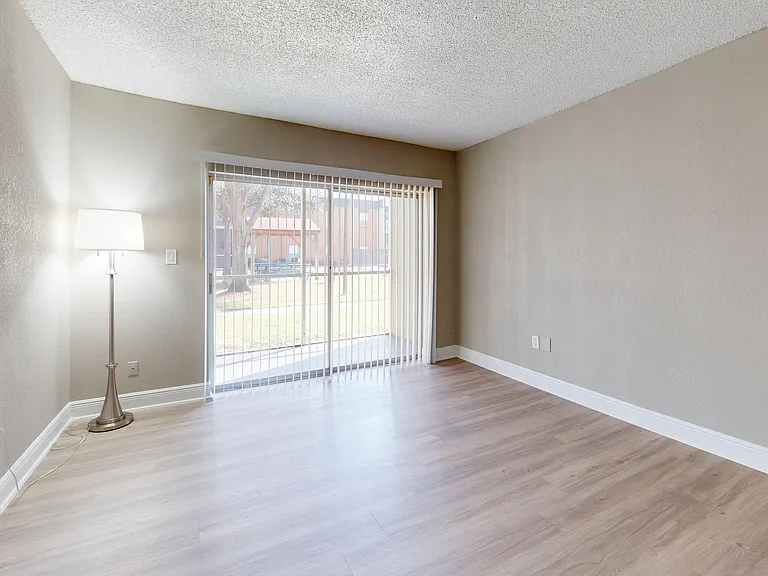 Bright and inviting living room with sleek wooden flooring, modern floor lamp, and expansive sliding glass patio doors opening to scenic outdoor views.