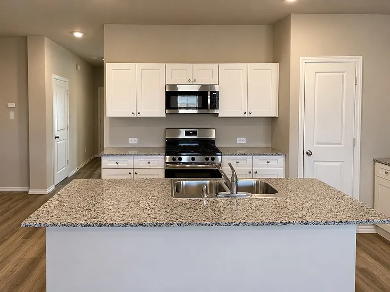 Kitchen featuring a center island with a double basin sink, light-toned granite countertops, white cabinetry, stainless steel appliances, and wood-finish flooring