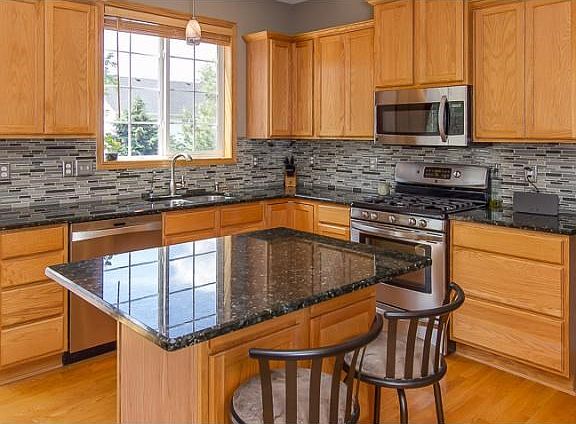 A closer view of the kitchen, showing the granite countertops, tiled backsplash and stainless steel appliances.