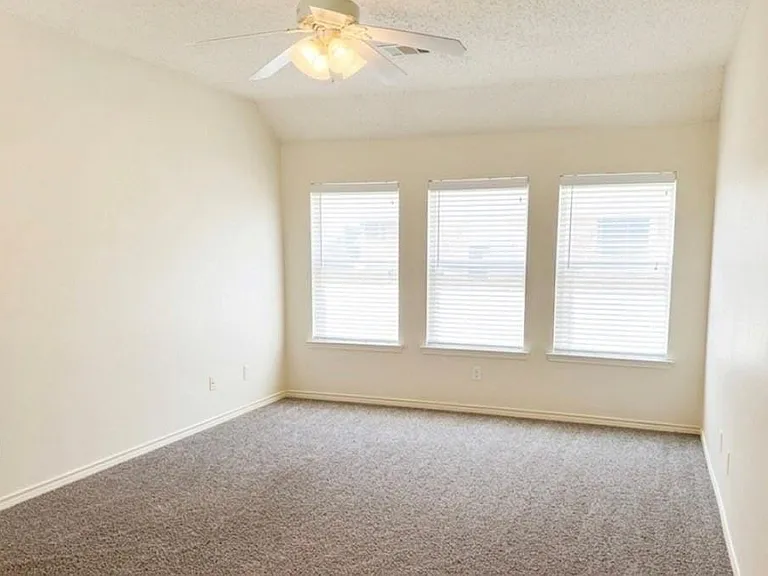 Spacious room featuring three windows with blinds, light-toned walls, and dark flecked carpeting