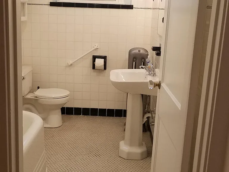 Pedestal sink and wrap-around shower curtain for original tub and restored tub surround with new bath faucet.