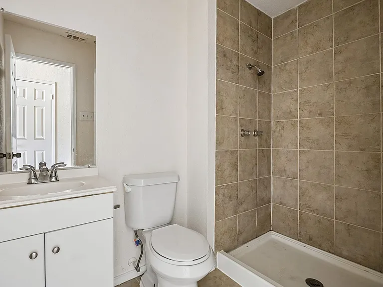 Bathroom featuring a vanity with an integrated sink, a commode, a walk-in shower with tile surround, and a wall-mounted mirror