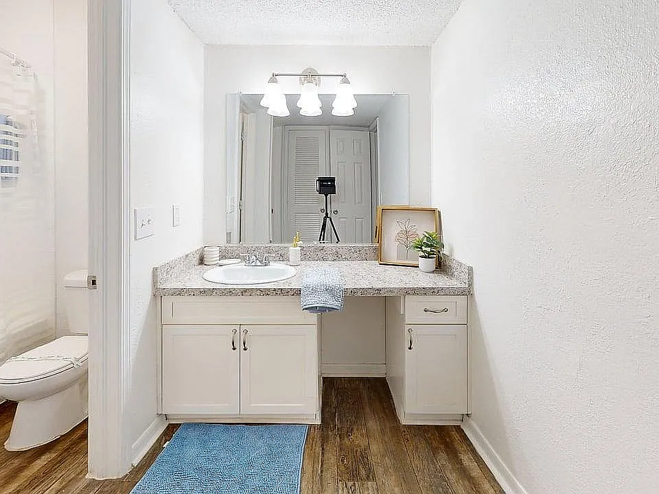 Bright and modern bathroom featuring a sleek vanity with granite countertop, stylish lighting, and elegant wood flooring.