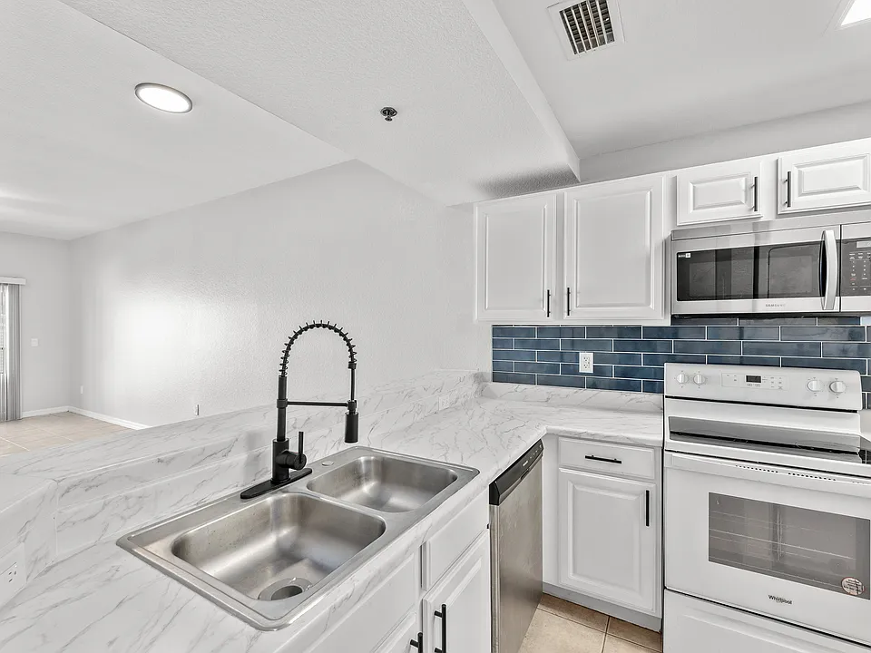 Modern kitchen featuring sleek white cabinetry, elegant marble countertops, stainless steel appliances, and a stylish dark faucet.