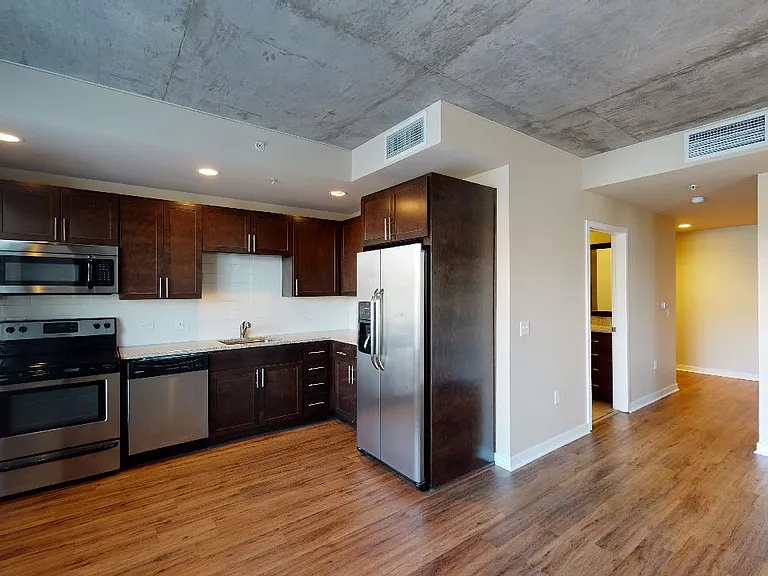 Apartment kitchen with stainless steel appliances, dining and living room with wood-style flooring.