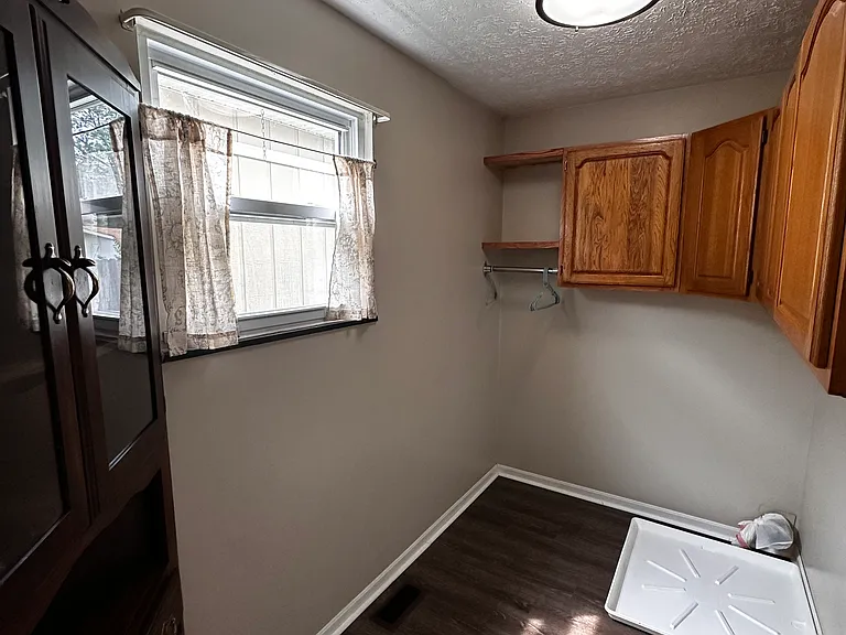 Utility with connections for a washer and electric dryer. There are cabinets for storage, a clothes hanging rod, and a corner storage built-in with glass doors a drawer and small shelf.