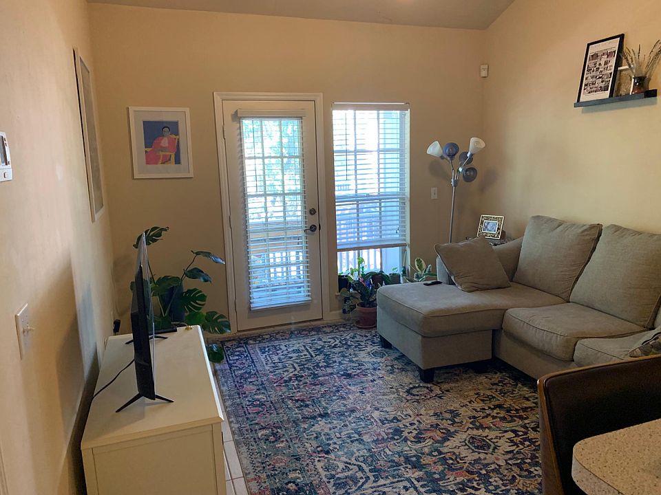 Living room with vaulted ceiling, tile floor, open to kitchen, door to balcony.