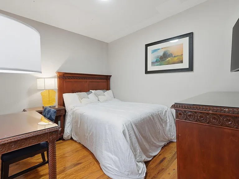 Queen bed, carved wood headboard, matching dresser, TV, and a workspace on hardwood floors.