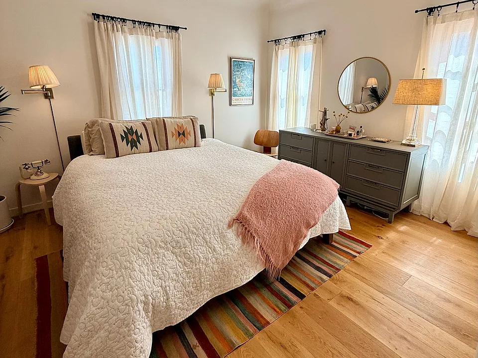 Light-drenched primary bedroom features a Cal king bed, Four Seasons mattress, flat-screen TV with Apple TV, Sonos speaker, large dresser, air purifyer and seating area.