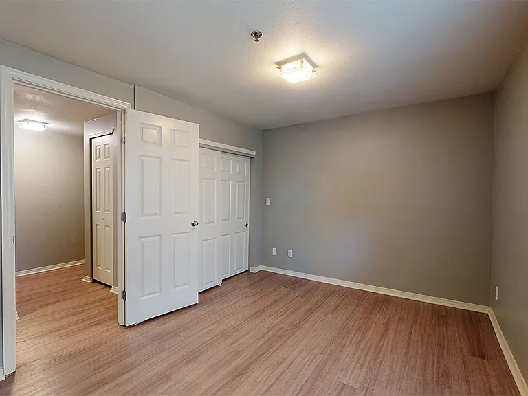 Spacious apartment bedroom with attached bathroom and wood-style flooring.