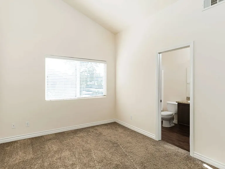 Carpeted bedroom with cathedral ceiling, larage window and bathroom at The Nines Townhomes in Escondido, California.