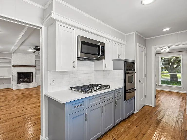 Kitchen featuring light wood-finish flooring, two-tone cabinetry with white upper and gray lower cabinets, a gas cooktop, built-in oven, and a stainless steel microwave