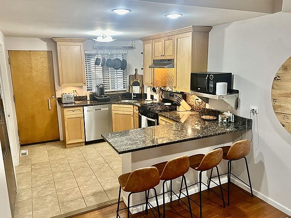 Kitchen with peninsula, tiled backsplash with under-cabinet lighting, granite countertops, stainless appliances.