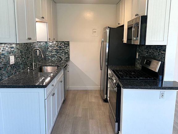 Gourmet kitchen with tons of white soft close cabinets, blue granite underlit counters with beach glass backsplash and a top chrome appliance package featuring gas range/oven, microwave, dishwasher & smart refrigerator/freezer