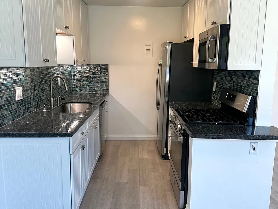 Gourmet kitchen with tons of white soft close cabinets, blue granite underlit counters with beach glass backsplash and a top chrome appliance package featuring gas range/oven, microwave, dishwasher & smart refrigerator/freezer