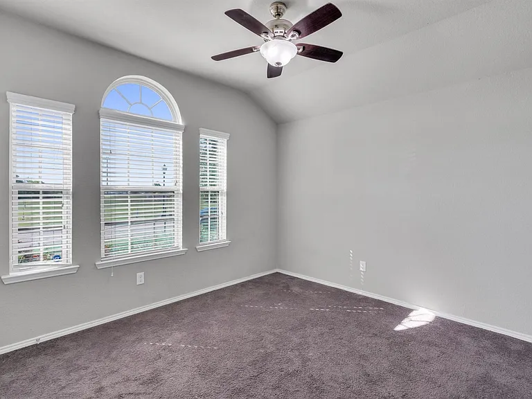 Room featuring vaulted ceilings, a ceiling fan with light kit, three windows with white blinds, an arched transom window, and gray carpet flooring