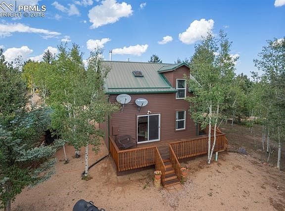Back side of home shows the deck, metal roof and satellite dishes along with the beautiful trees
