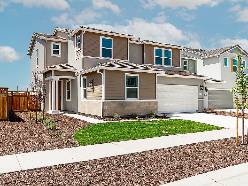 A two-story residential house with a well-manicured lawn, surrounded by a paved driveway and a woode