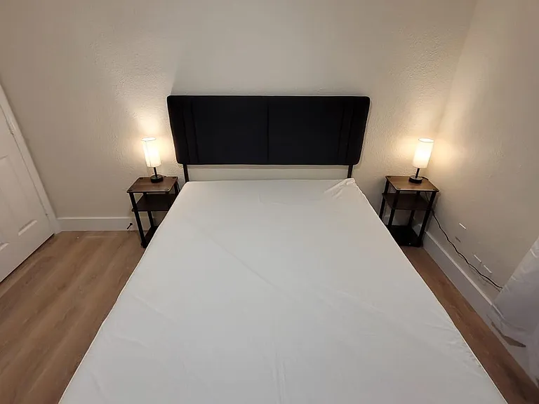 Bedroom with a full-size bed, upholstered headboard, matching nightstands, and bedside lamps on durable wood-look flooring.