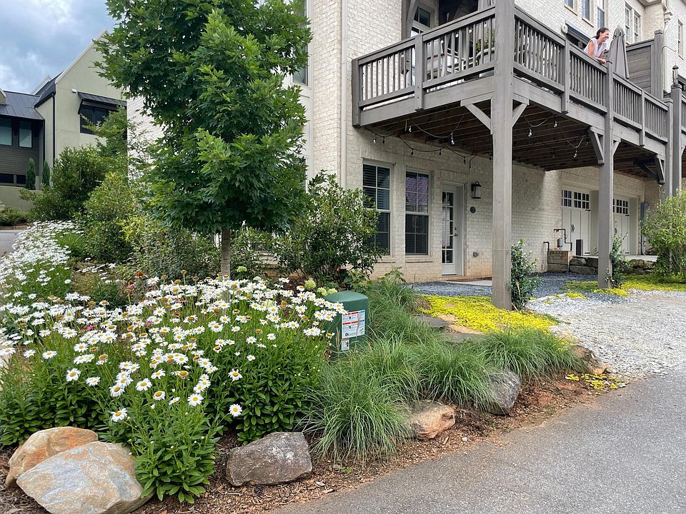 Shaded, slate-chip patio nestled in verdant landscaping with gravel parking pad right outside