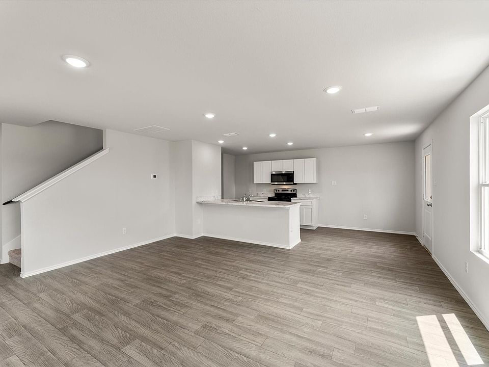 Open-concept living space featuring wood-finish flooring, recessed lighting, and a white kitchen with a peninsula island