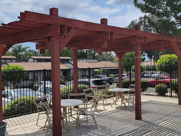 Sun deck with a wooden pergola, tables, and chairs around the pool area.