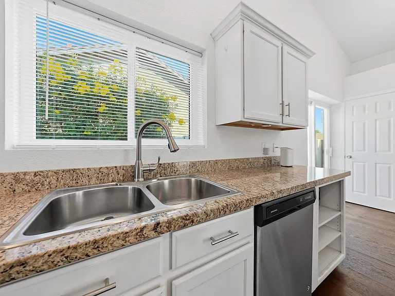 Kitchen workspace features a double-basin stainless sink, granite-look counters, and ample cabinetry with window light.